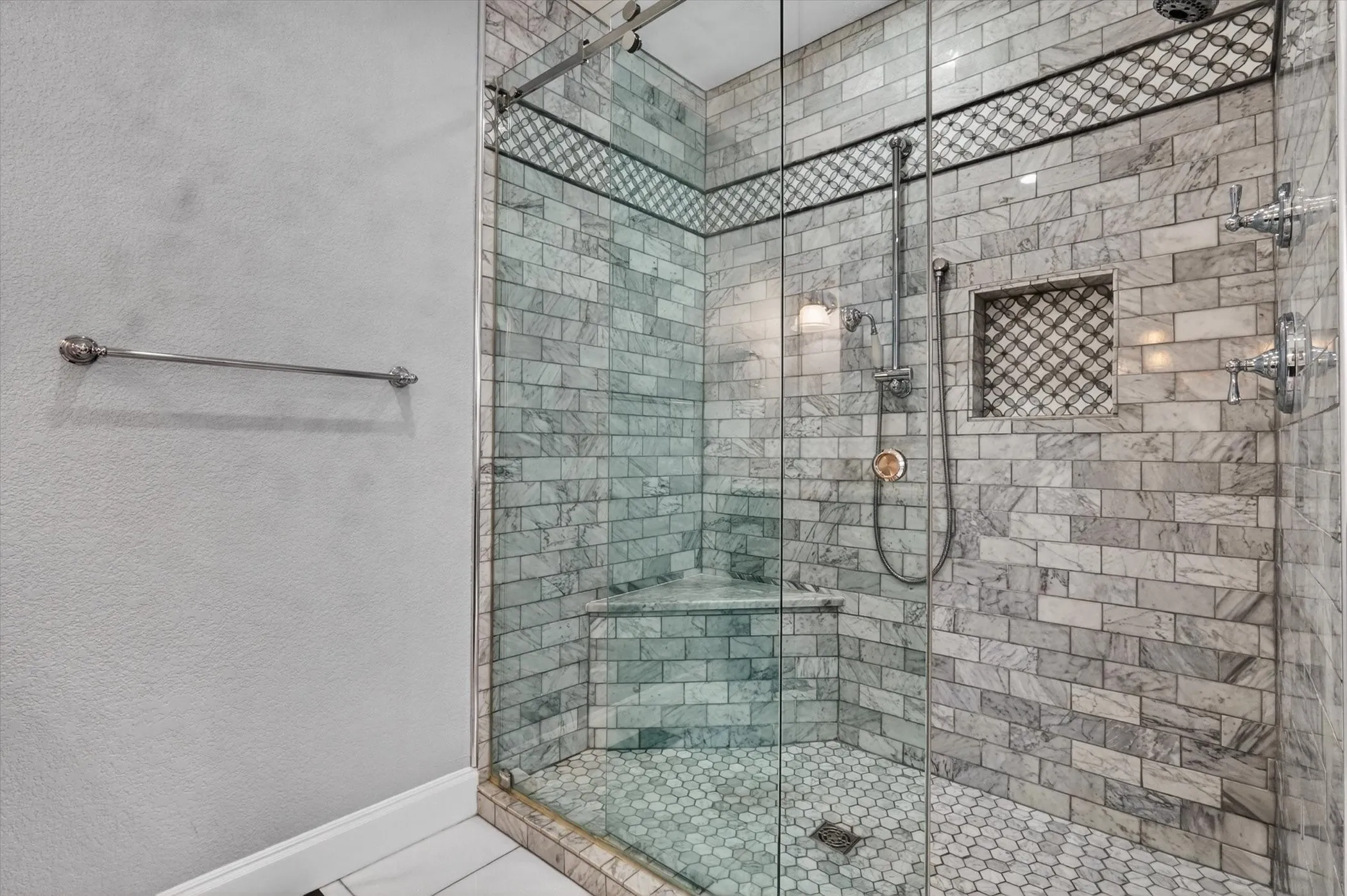 Glass-enclosed shower featuring subway tile walls, a decorative mosaic tile accent band, and a convenient corner bench