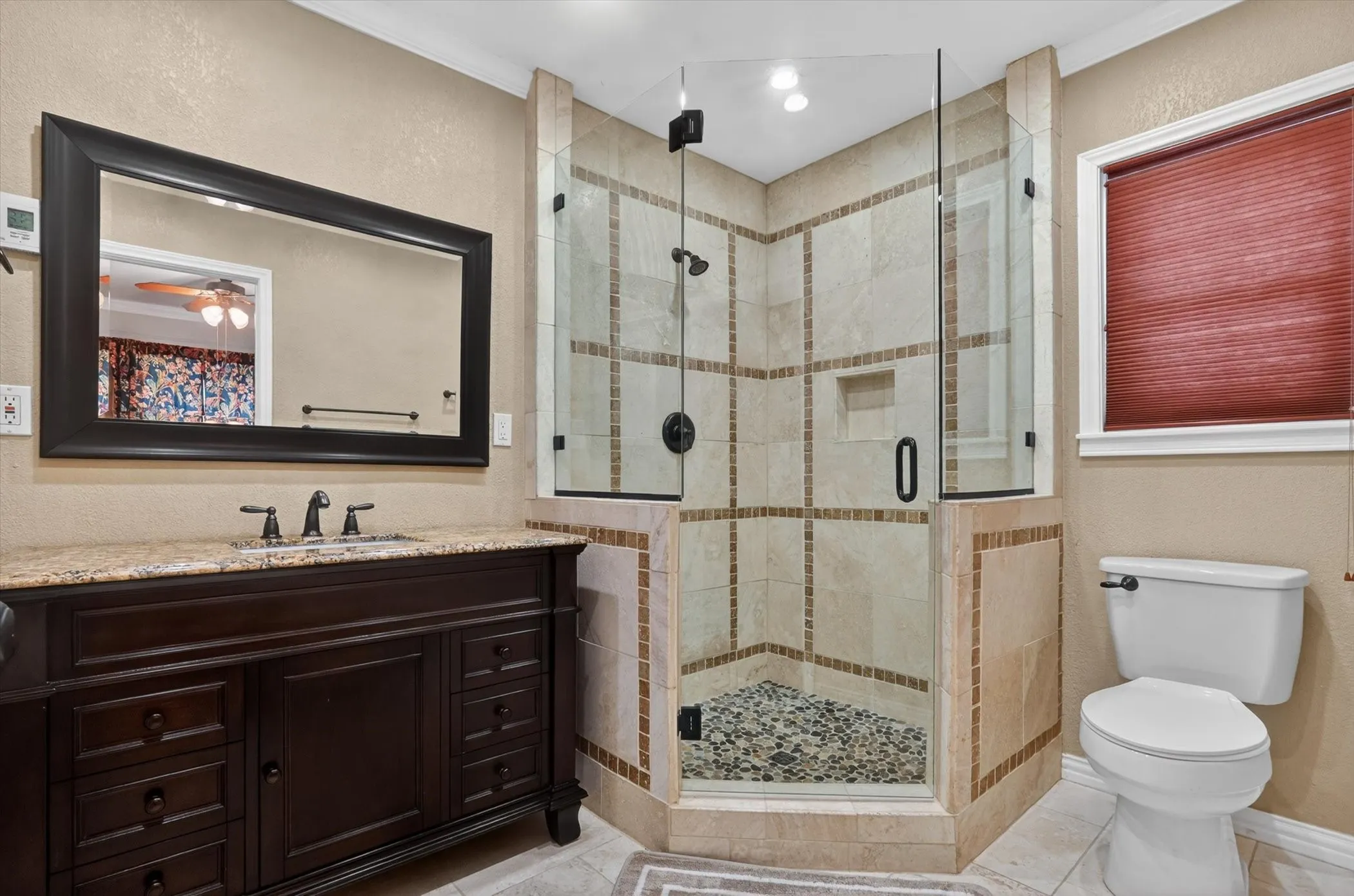 Bathroom featuring a corner glass-enclosed shower with a river rock floor, a built-in shower niche, and tiled walls