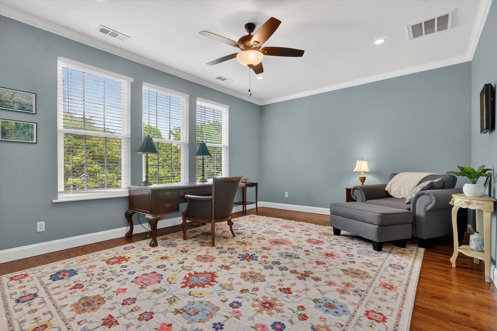 Spacious room featuring multiple windows, crown molding, a ceiling fan with integrated lighting, recessed lighting, and wood-finish flooring