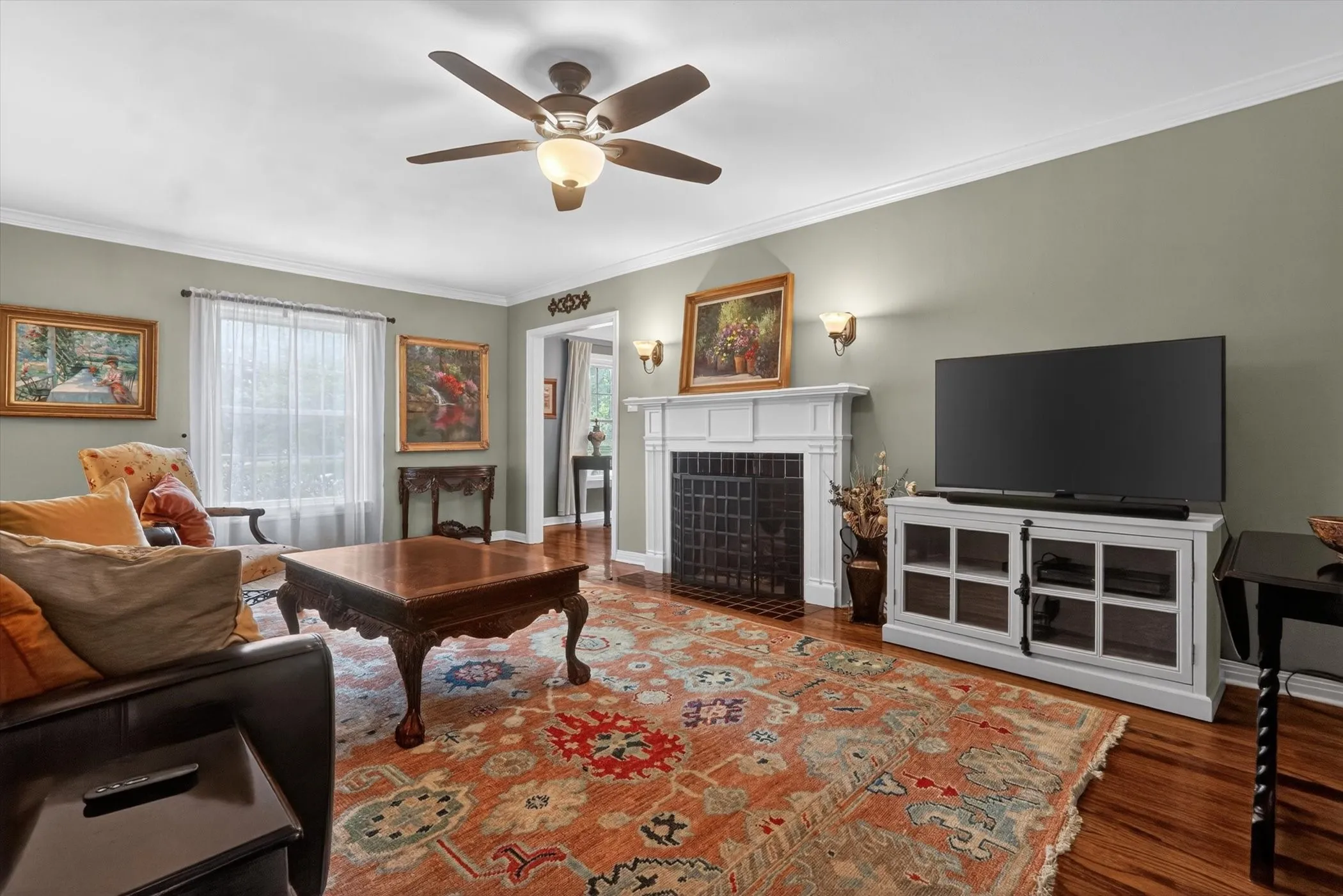 Living area featuring wood-finish flooring, a white mantel fireplace with a black grate, and crown molding