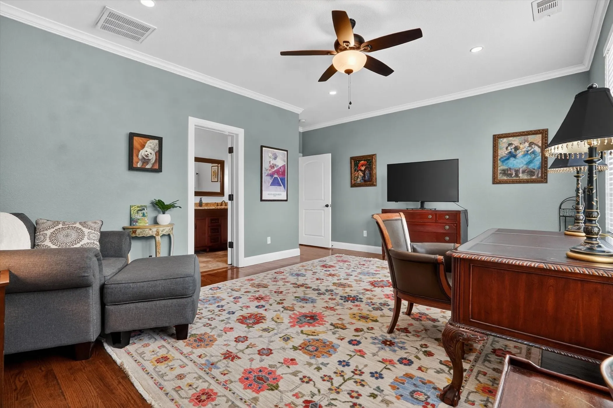 Spacious room featuring rich wood-finish flooring, light blue walls with white crown molding, and a ceiling fan with integrated lighting