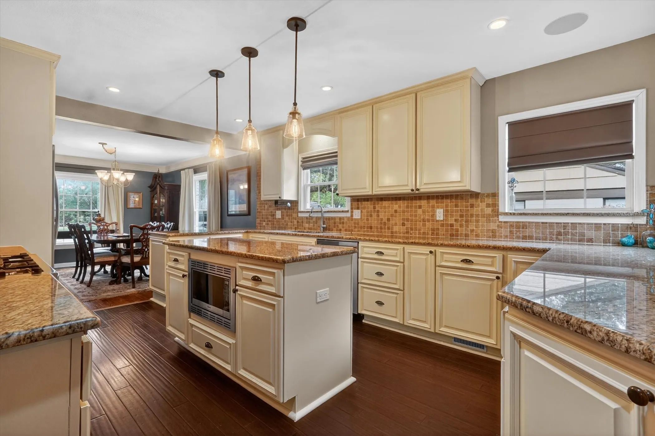 Kitchen featuring wood-finish flooring, cream-colored cabinetry, a large center island with built-in microwave, and pendant lighting