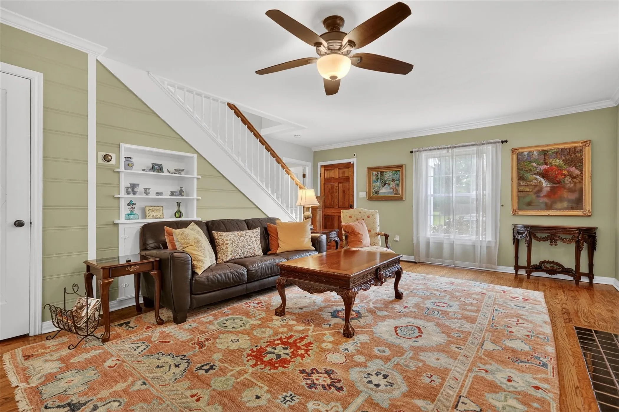 Living area featuring wood-finish flooring, a ceiling fan with integrated lighting, and a window with sheer curtains