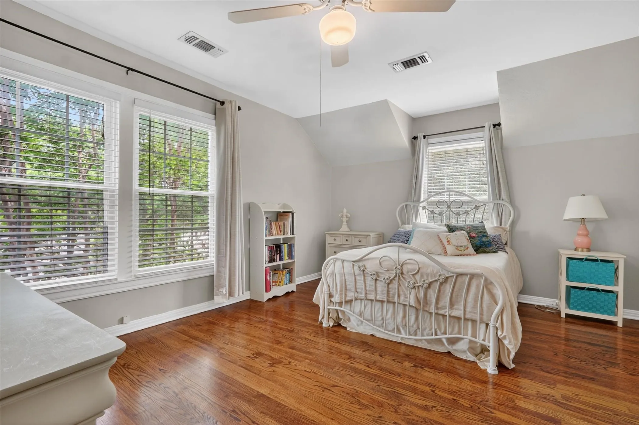 Hardwood flooring throughout featuring two large windows, a ceiling fan with light fixture, and a built-in bookshelf