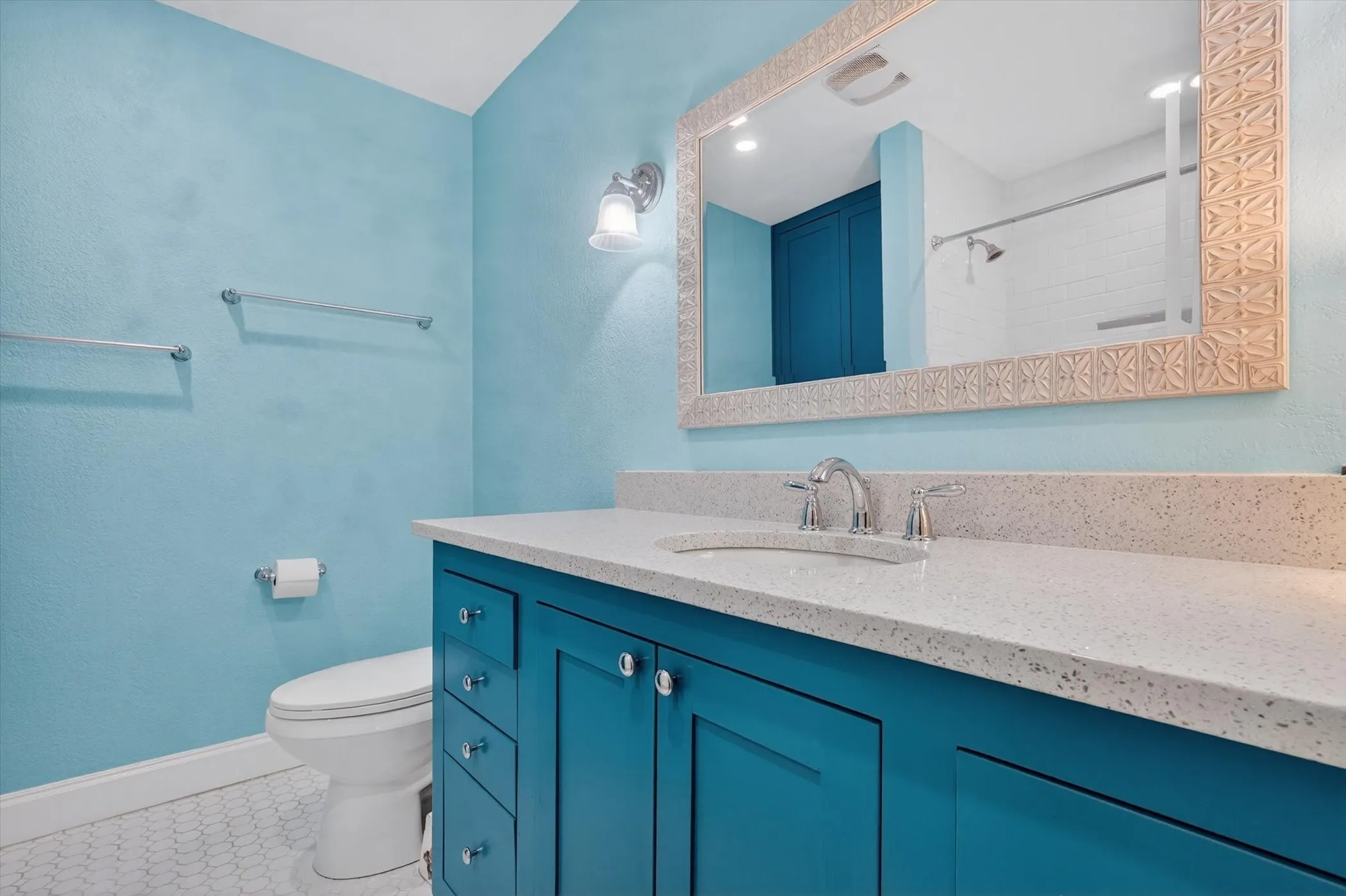 Bathroom featuring a teal vanity with an integrated sink, polished chrome faucet, and a light-toned speckled countertop