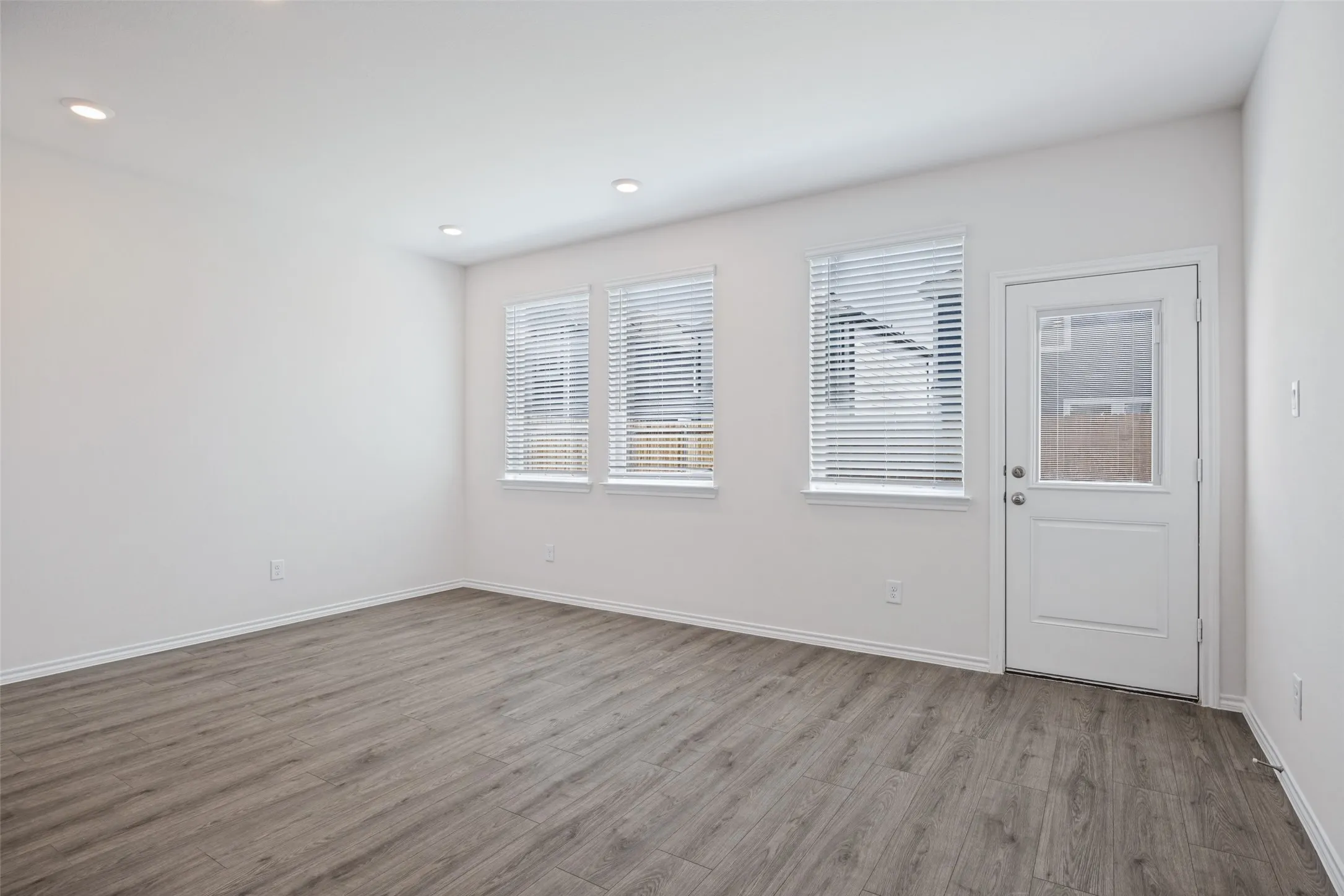Recessed lighting, wood-finish flooring, white walls, multiple windows with blinds, and an exterior door with glass paneling