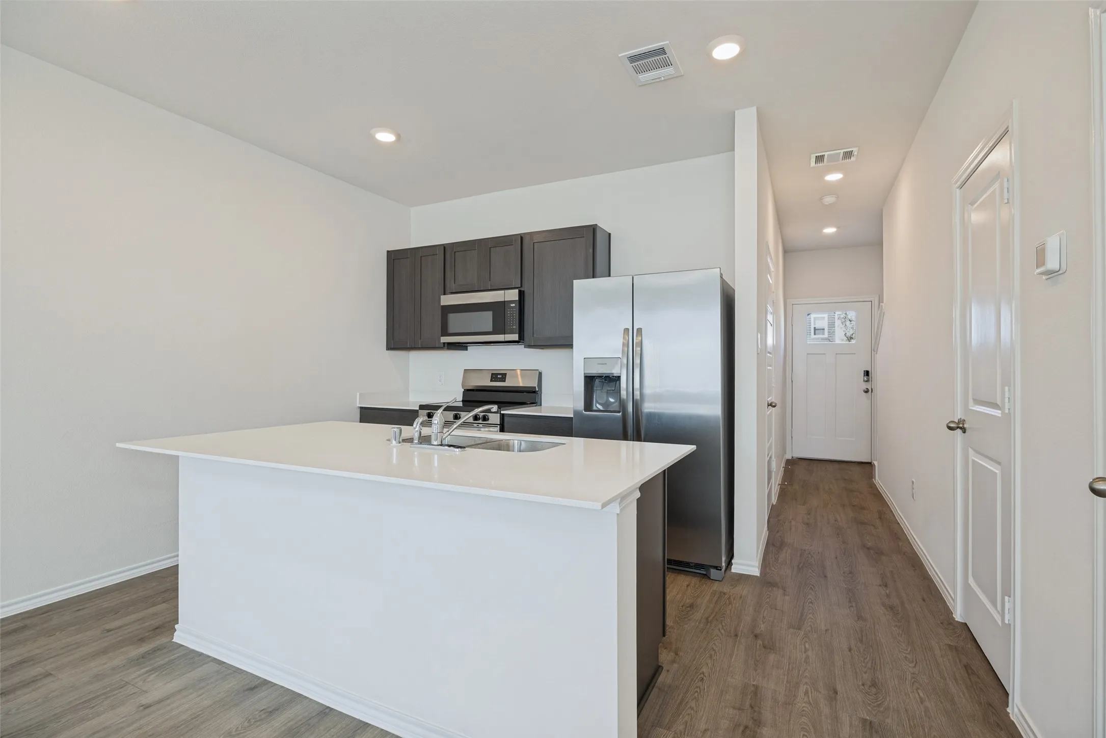 Kitchen island with white countertop, dark wood-finish cabinetry, stainless steel appliances, and wood-finish flooring