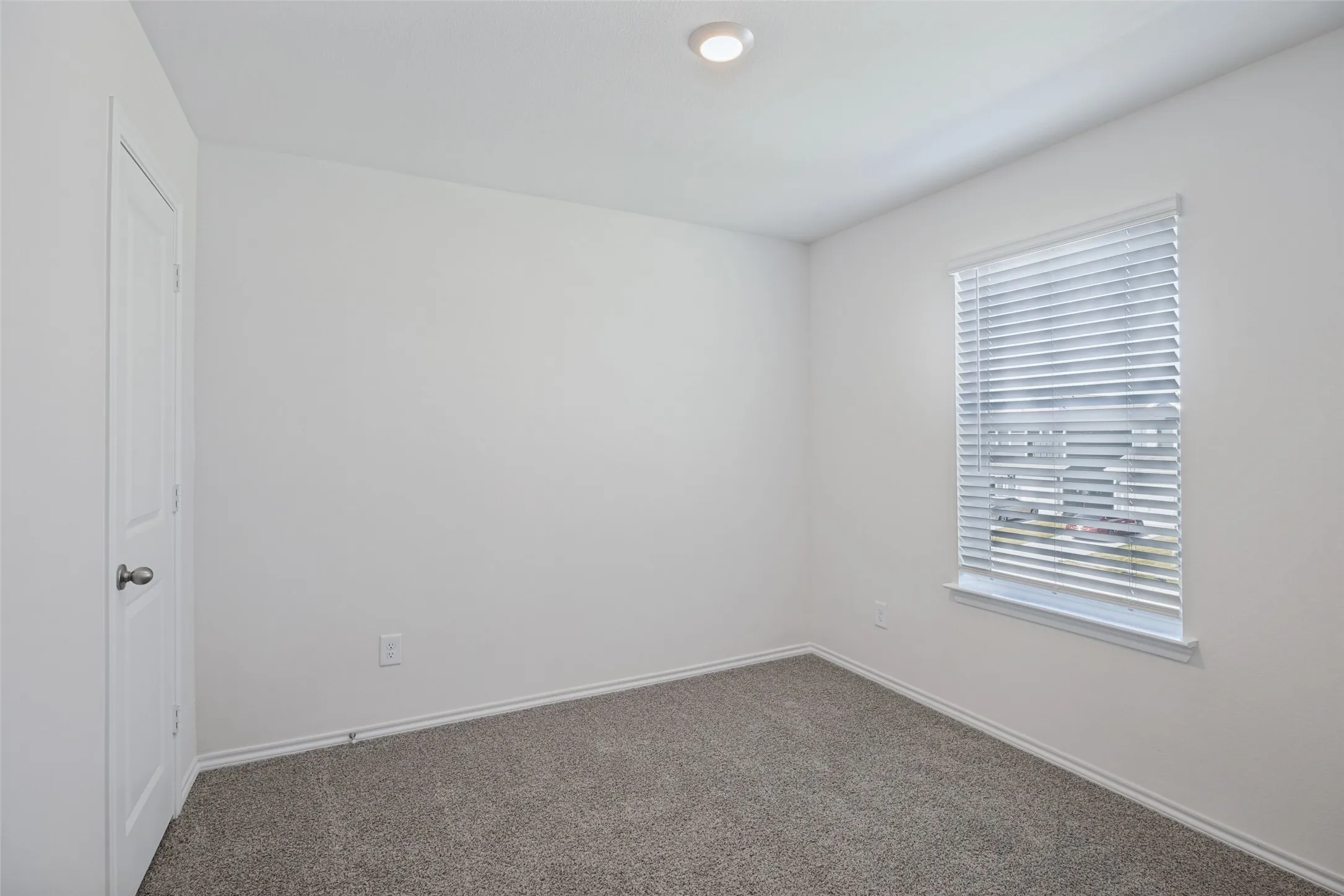 Recessed ceiling lighting, white interior walls, window with horizontal blinds, and gray carpet