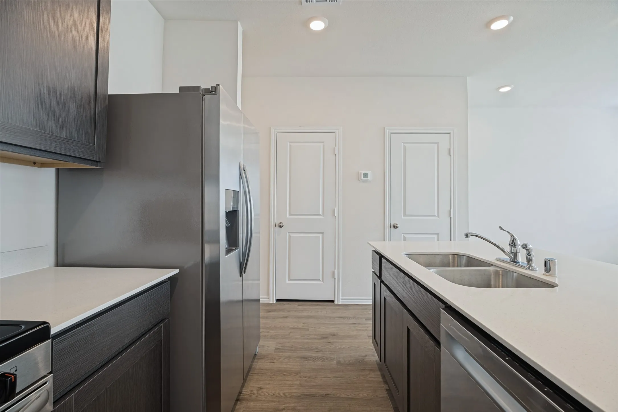 Kitchen featuring dark wood-finish cabinetry, light-toned countertops, a stainless steel refrigerator, and wood-finish flooring