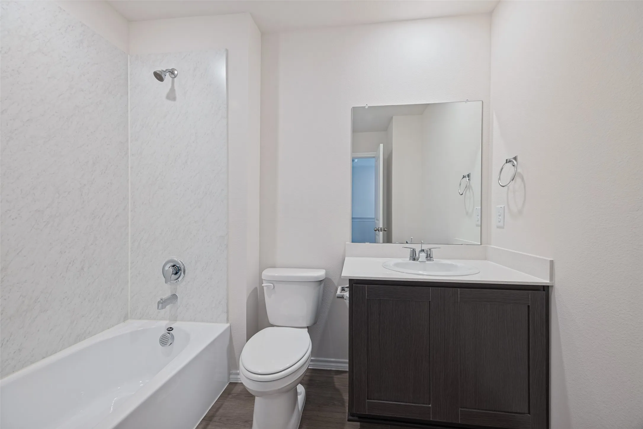 Bathtub with shower, toilet, dark wood-finish vanity with white countertop, and wall-mounted mirror
