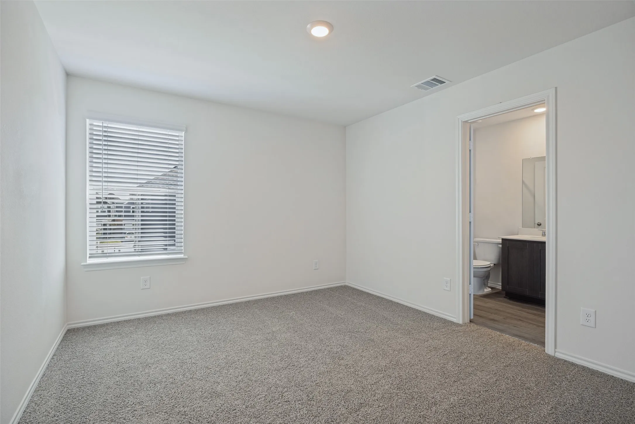 Carpeted room with a window, recessed lighting, and a doorway opening to a bathroom