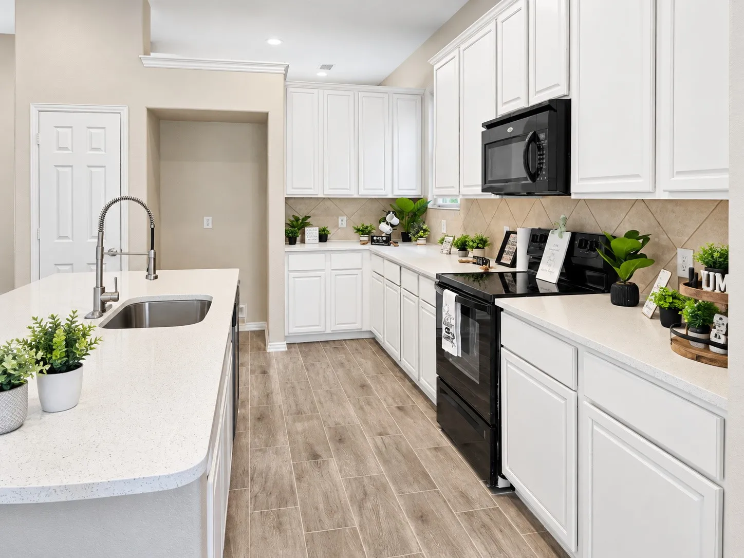 Kitchen with white cabinetry, white countertops, stainless steel sink, black appliances, and wood-finish flooring