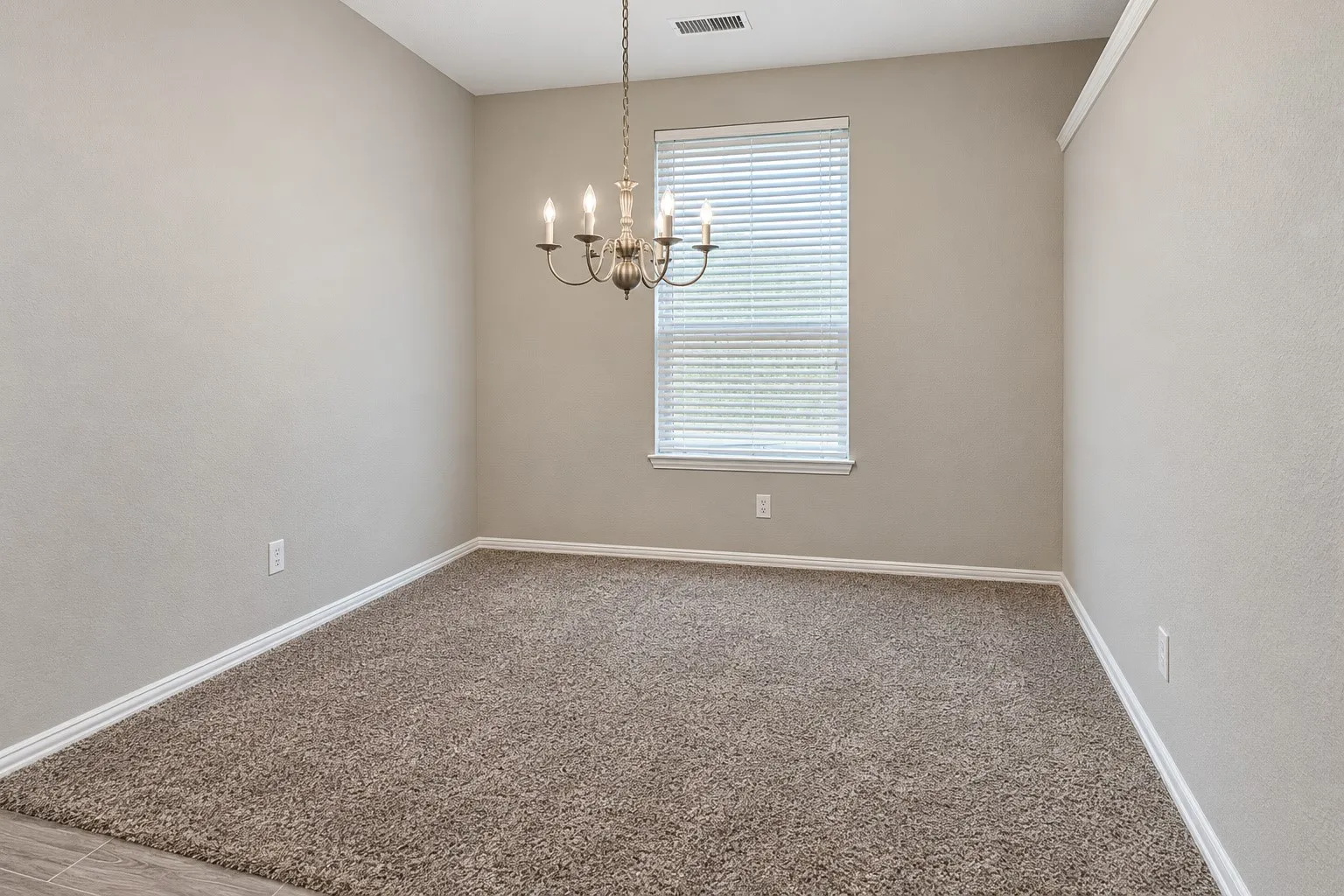 Neutral tone wall paint, textured carpeting, contemporary chandelier, window with blinds, and white trim