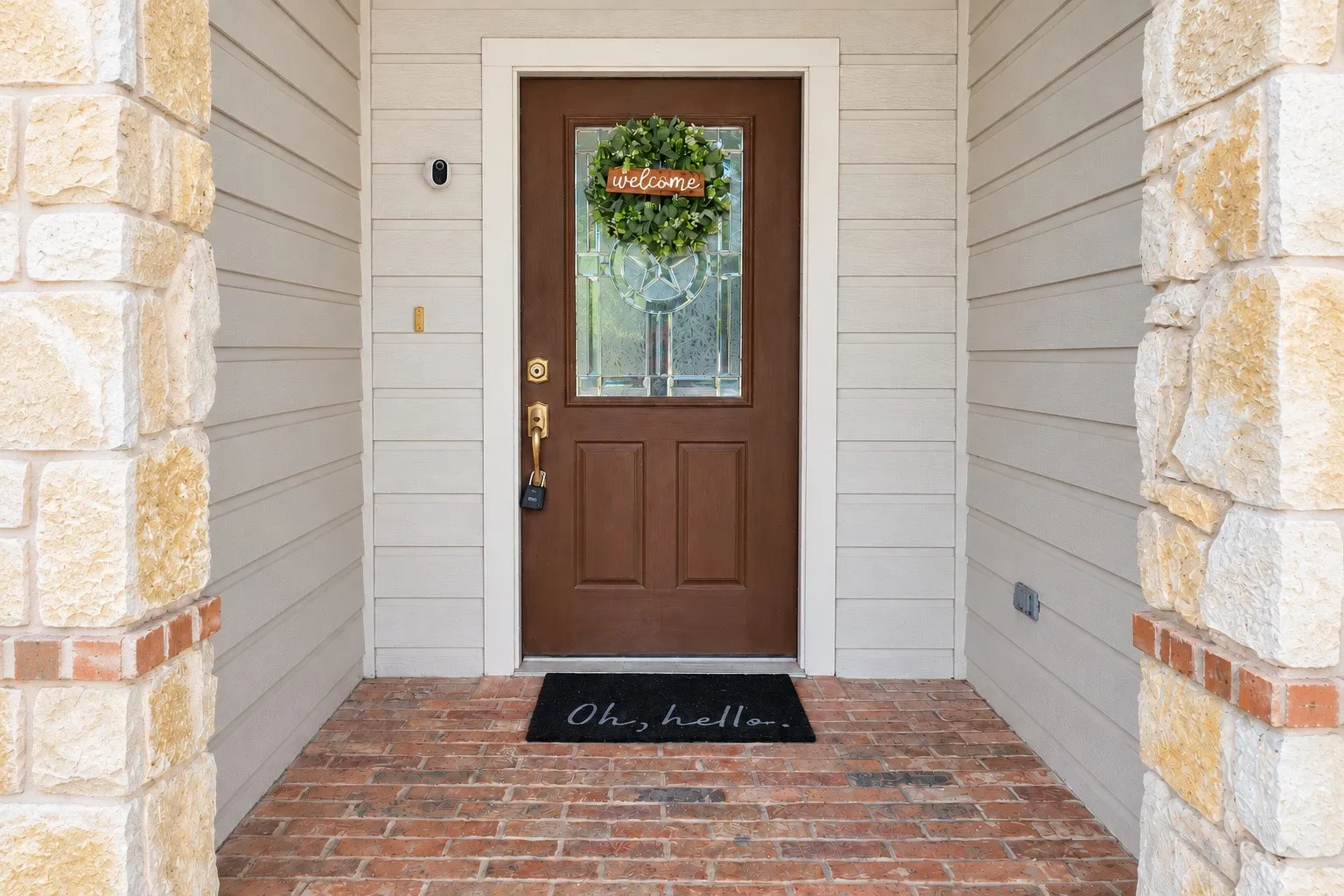 Entryway featuring stone columns, brick flooring, horizontal siding, and a wood-panel door with decorative glass