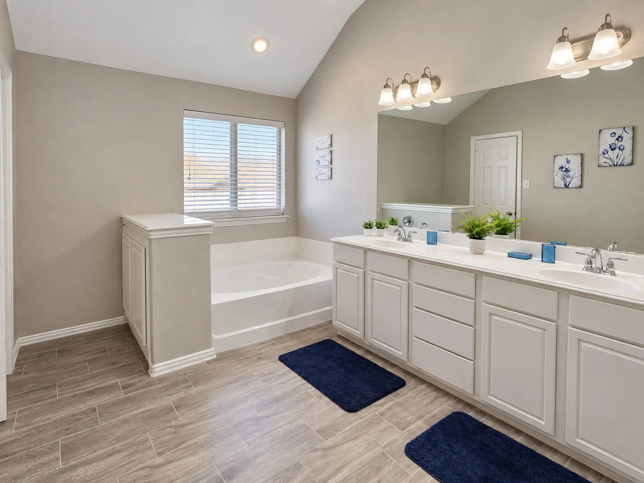 Double vanity with integrated sinks, a built-in soaking tub, wood-finish flooring, and a window with blinds