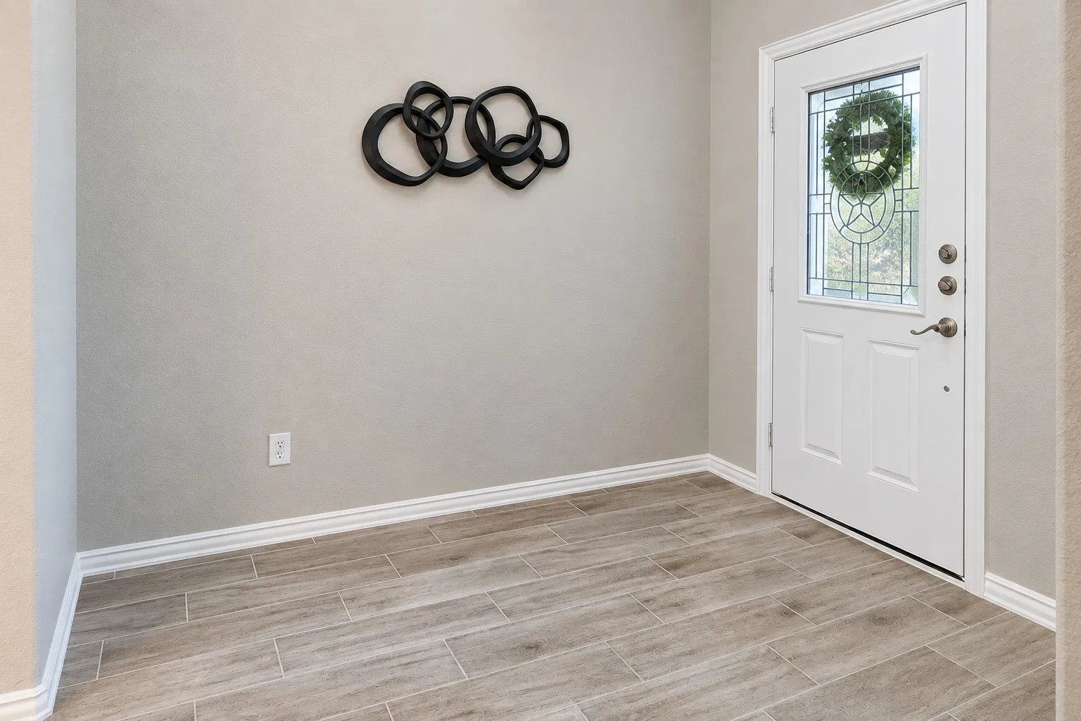 Entryway with wood-finish flooring, light neutral wall tones, and a white paneled door featuring decorative glass