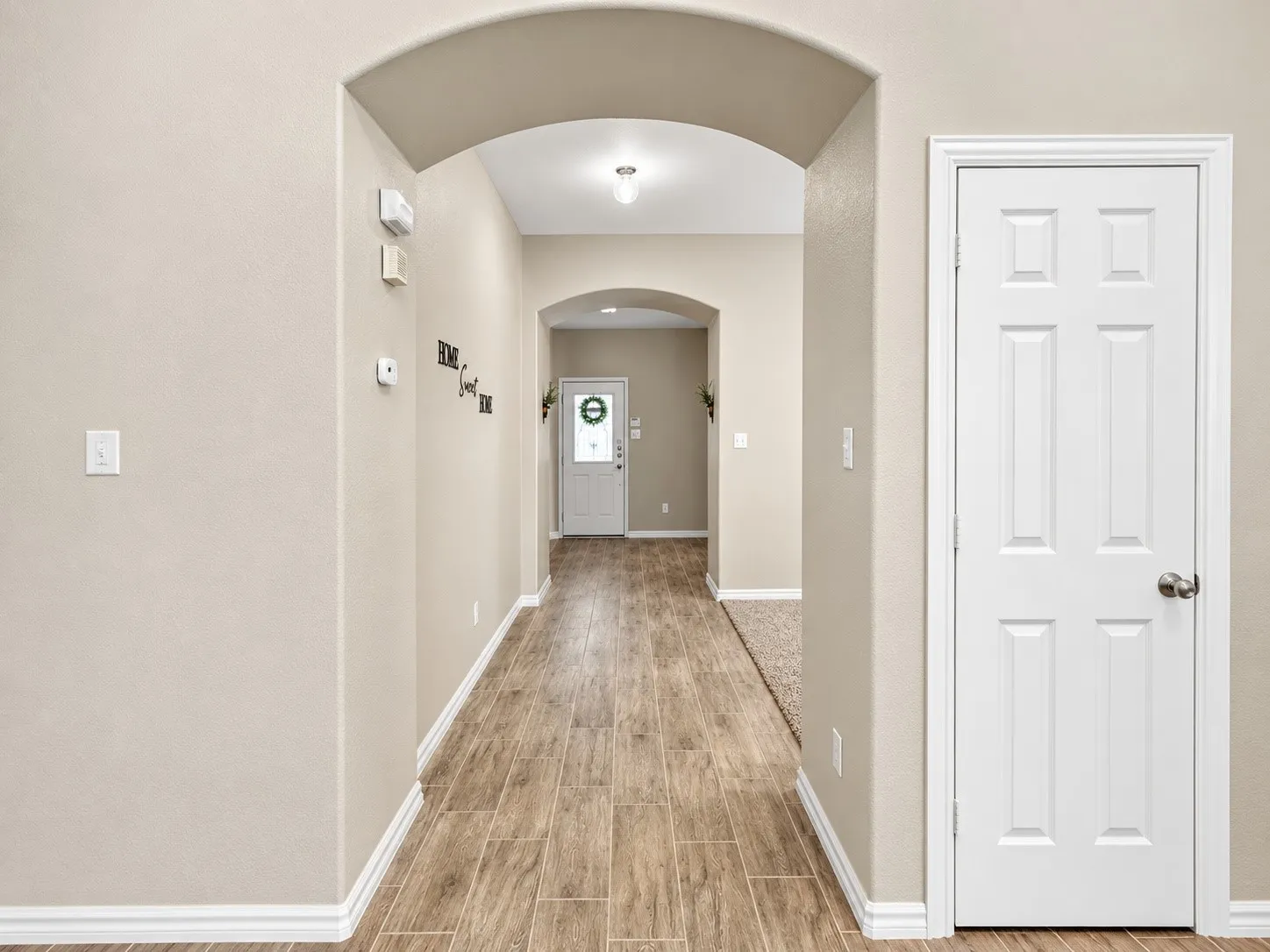 Arched entryway with wood-finish flooring, neutral wall tones, and bright white trim