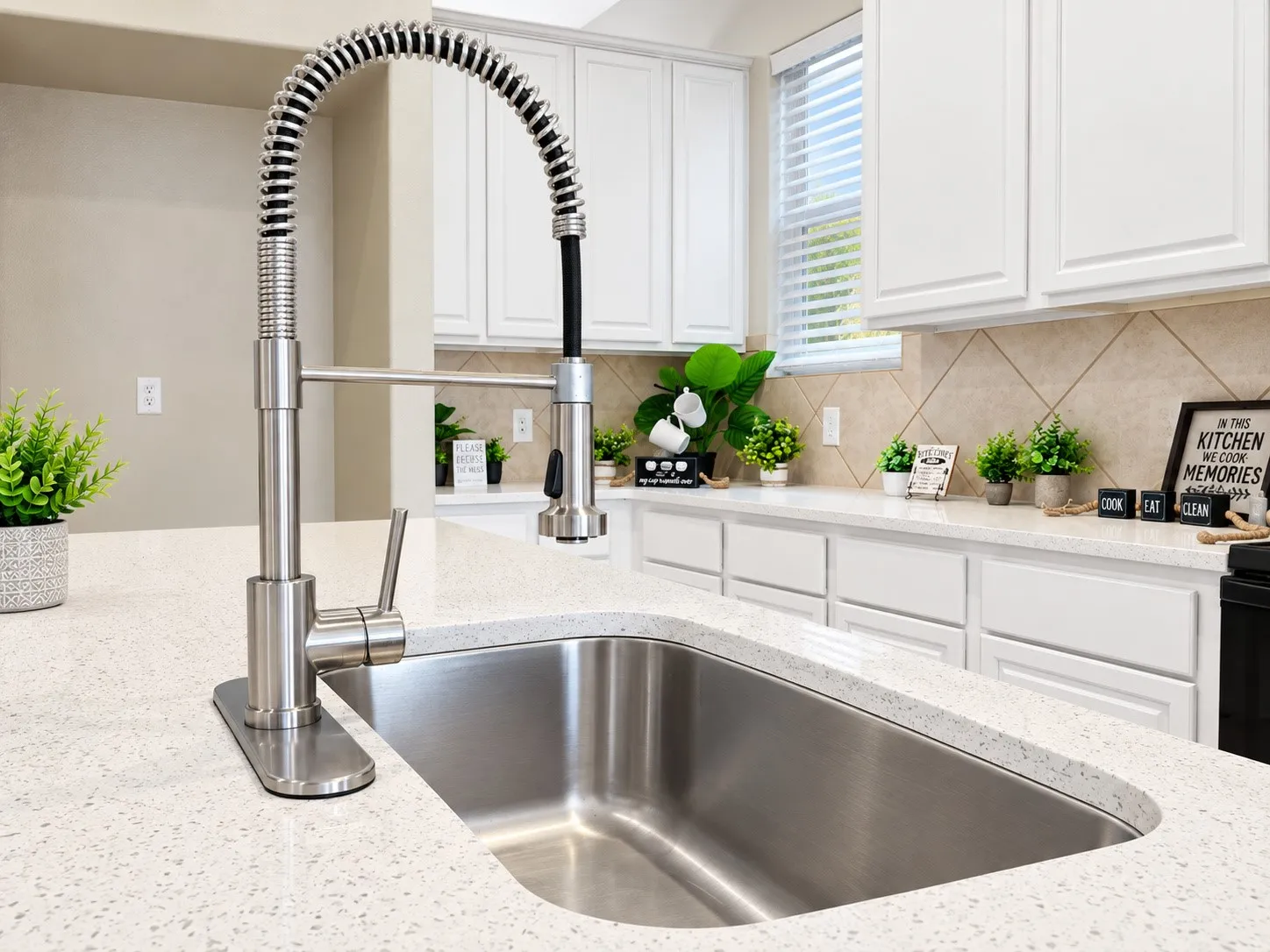 Stainless steel gooseneck faucet with an integrated sprayer, undermount stainless steel sink, light-toned countertops, white cabinetry, and tiled backsplash