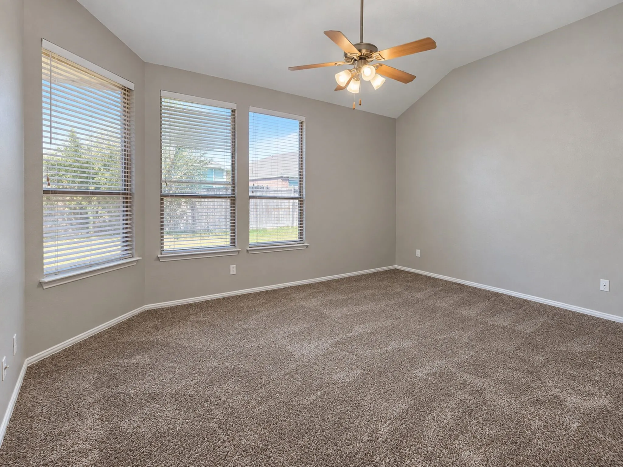 Vaulted ceiling with an attached ceiling fan, three large windows with blinds, and neutral-toned carpeting