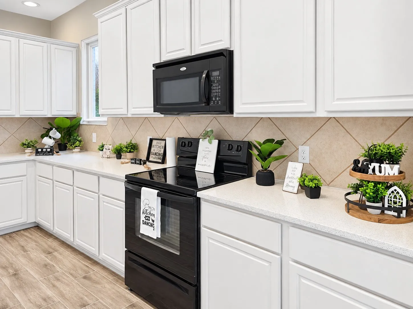 White cabinetry with black hardware, stone-finish countertops, diagonal tile backsplash, stainless steel microwave, and wood-finish flooring