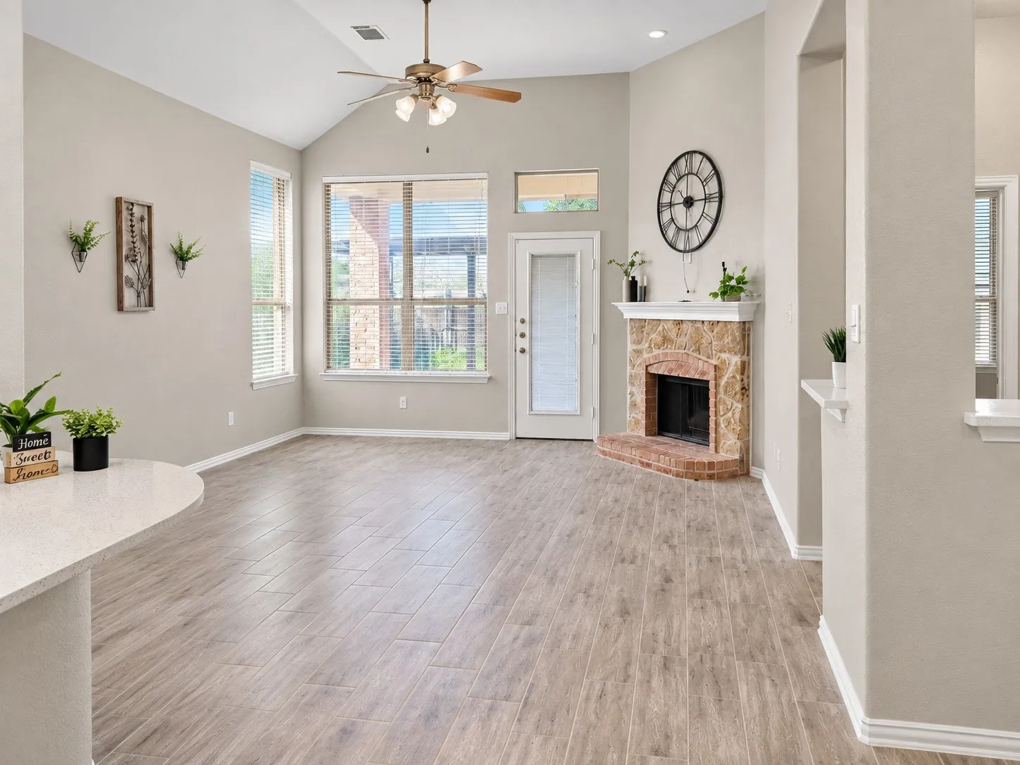 Vaulted ceiling, wood-finish flooring, corner fireplace with stone surround, ceiling fan, and transom windows