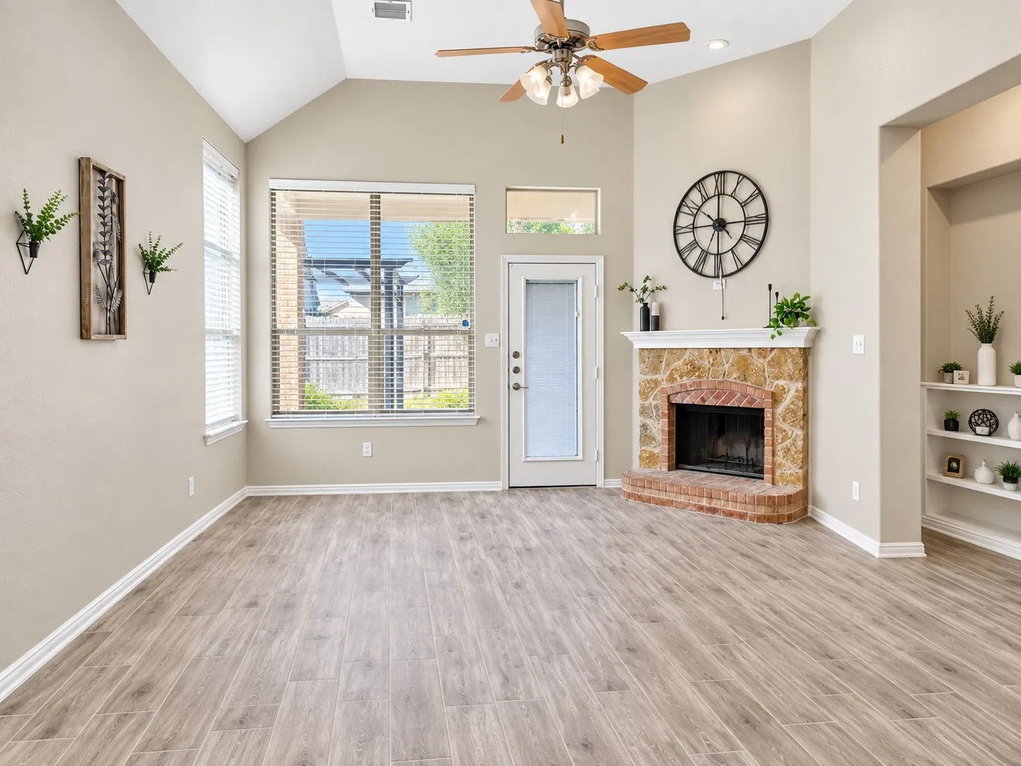 Vaulted ceiling, wood-finish flooring, corner fireplace with brick and stone surround, built-in shelving, and ceiling fan