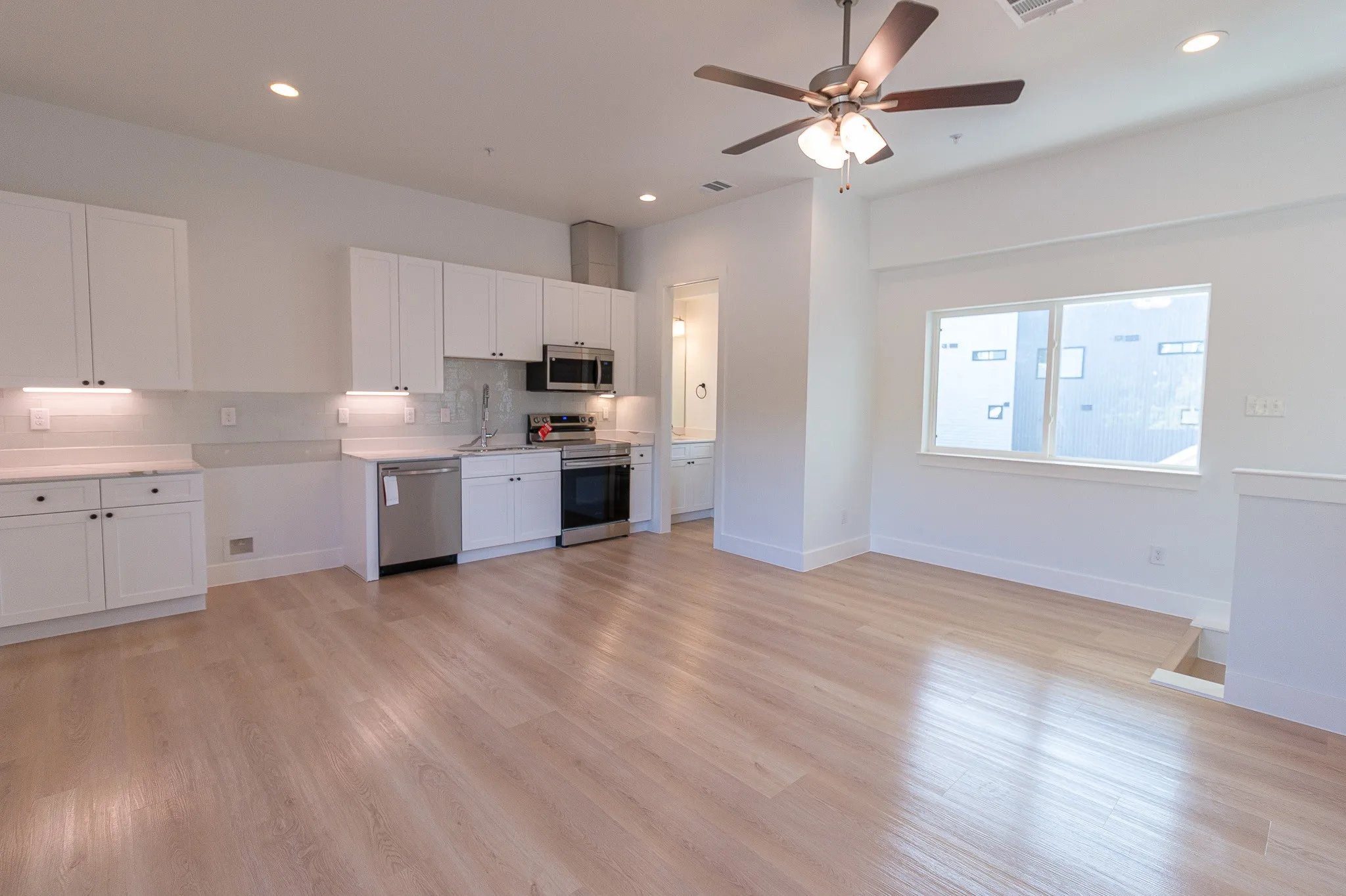 Kitchen with white cabinets, decorative backsplash, light wood-type flooring, and appliances with stainless steel finishes