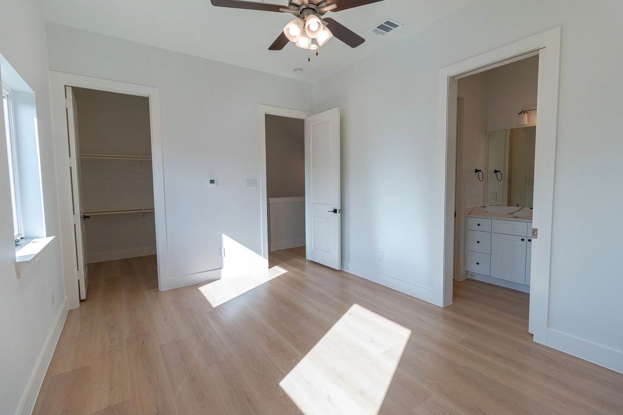 Unfurnished bedroom with ensuite bathroom, ceiling fan, a spacious closet, light hardwood / wood-style flooring, and a closet
