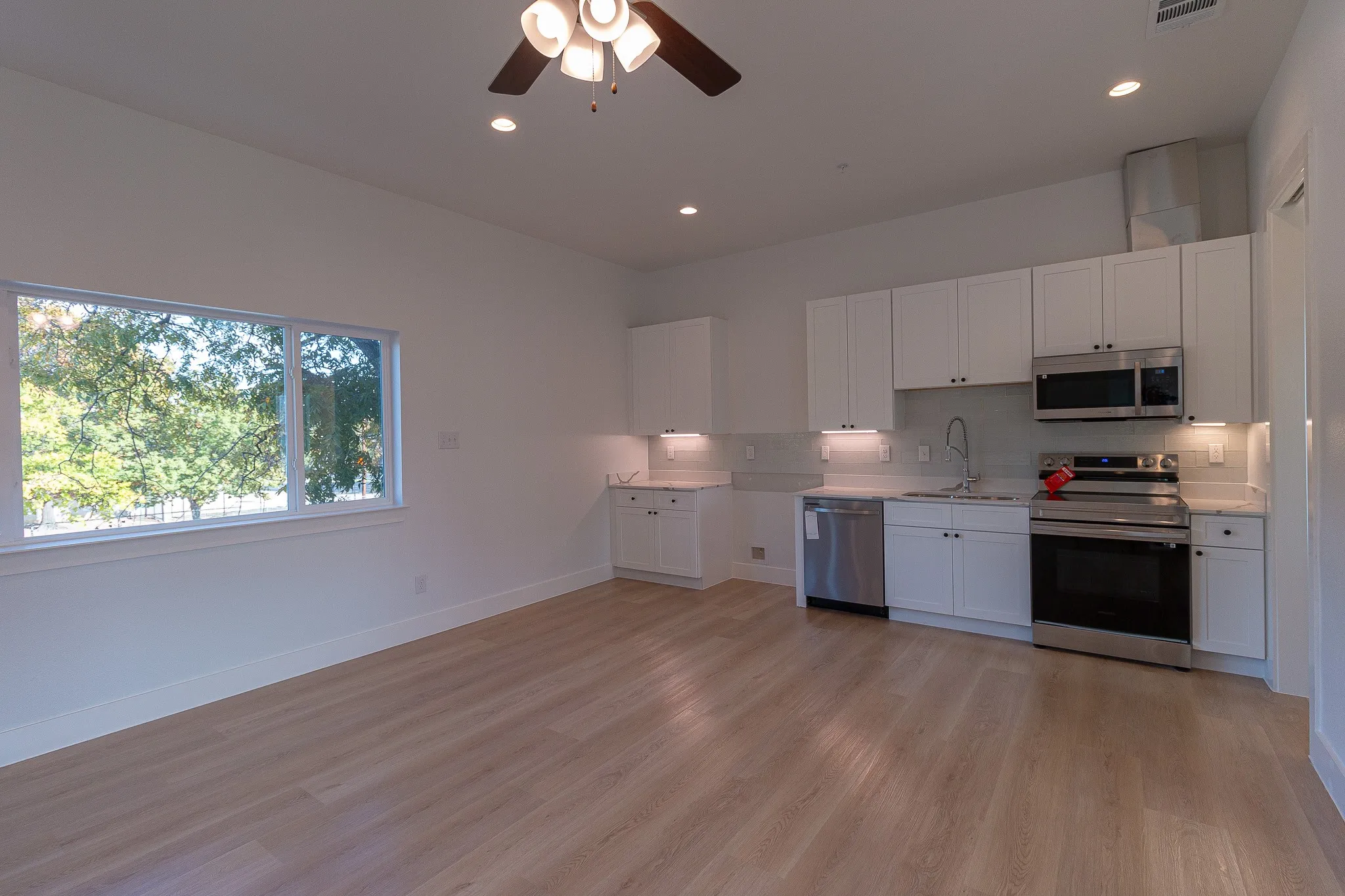 Kitchen with decorative backsplash, appliances with stainless steel finishes, light wood-type flooring, sink, and white cabinets