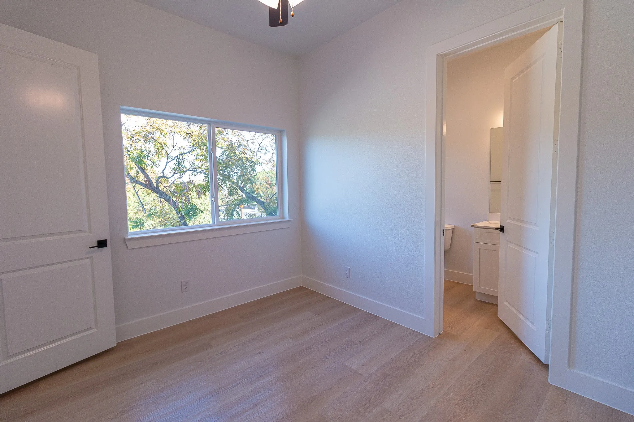 Unfurnished bedroom featuring connected bathroom, ceiling fan, and light hardwood / wood-style floors