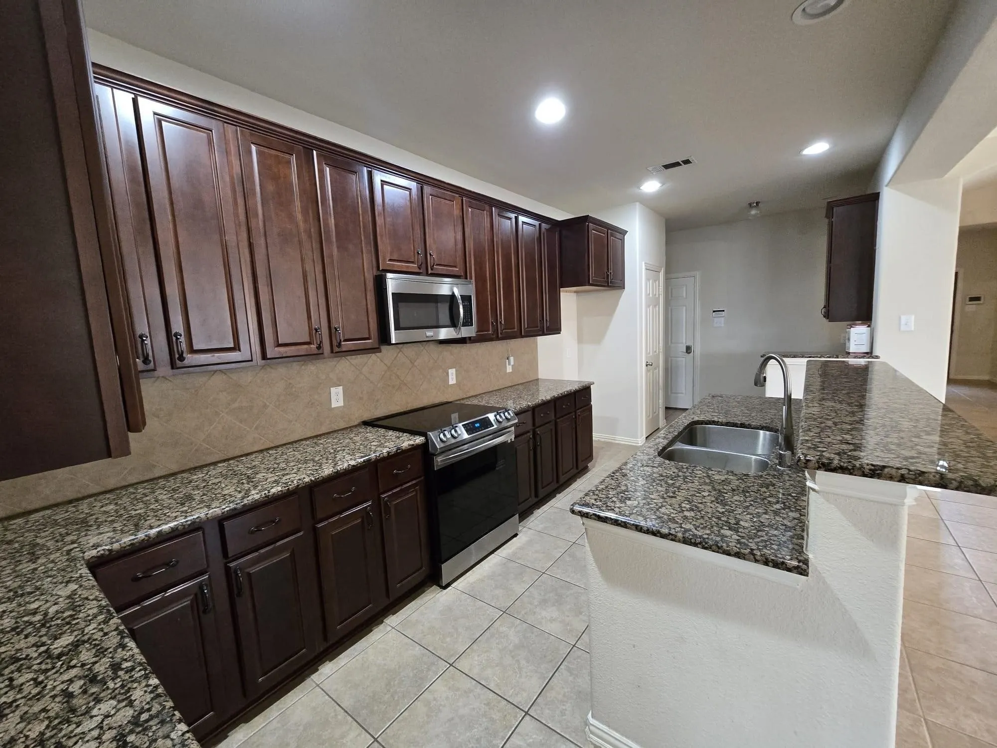 Kitchen with backsplash, dark stone countertops, sink, light tile patterned floors, and appliances with stainless steel finishes