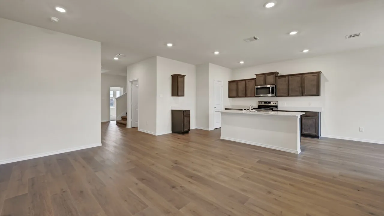 Open-concept living area with wood-finish flooring, recessed lighting, and a kitchen featuring dark wood cabinetry, stainless steel appliances, and an island with a light-colored countertop