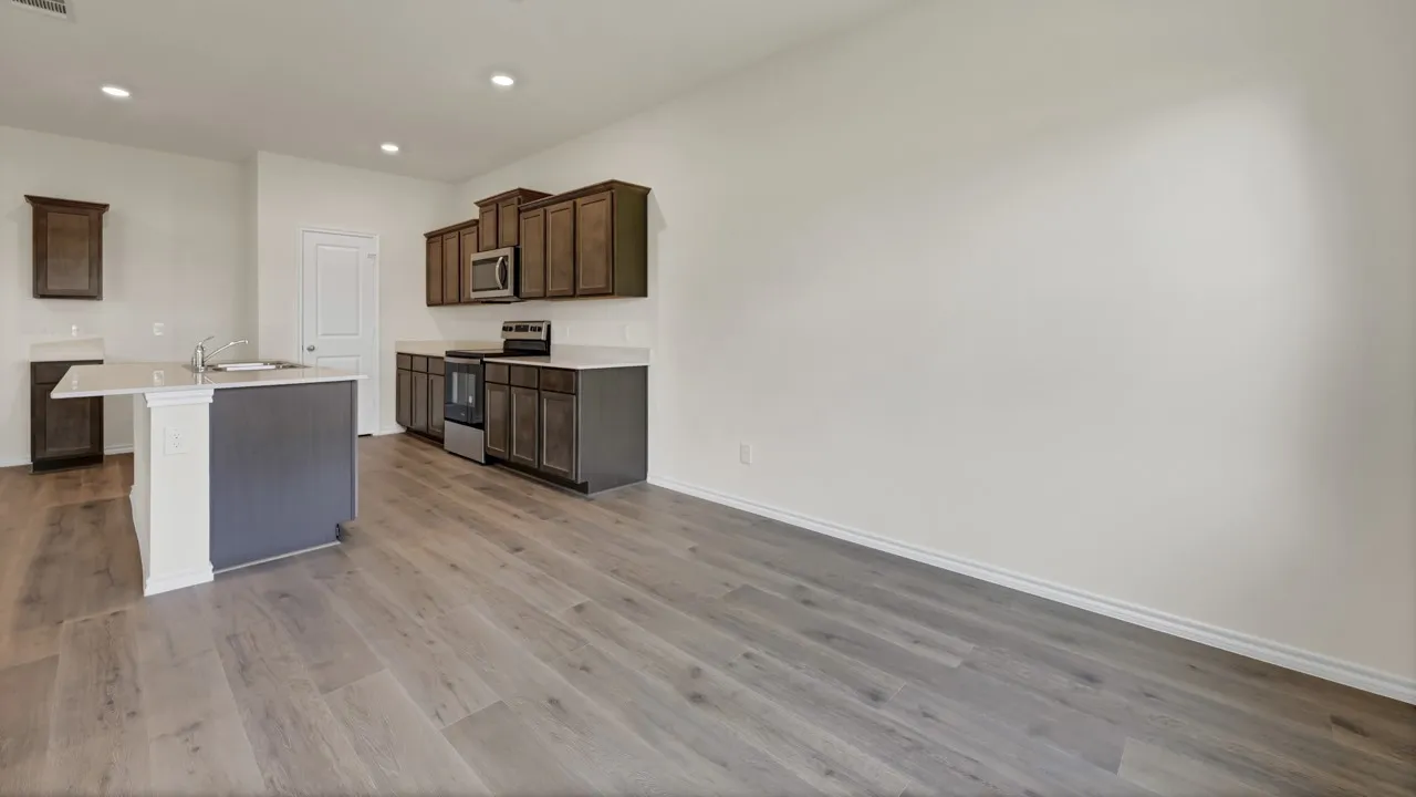 Modern kitchen featuring wood-finish flooring, dark wood cabinetry, and a central island with a sink and light-toned countertop