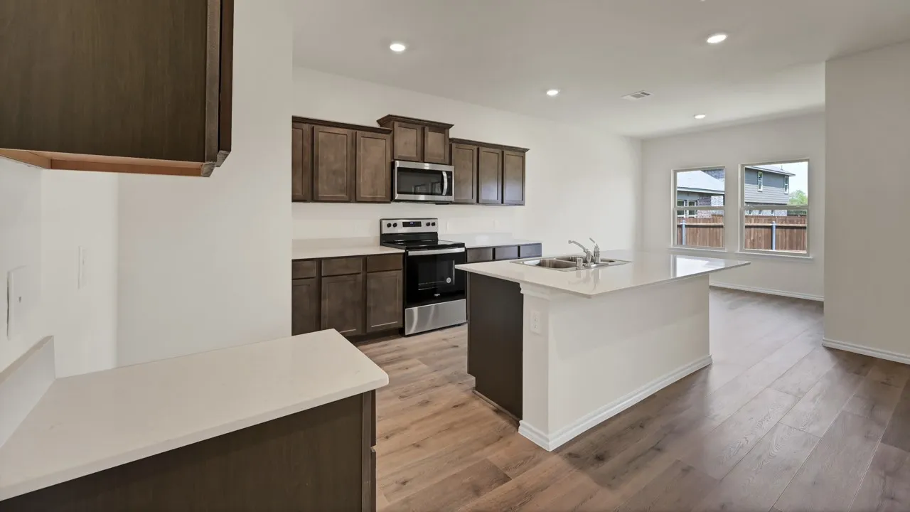 Modern kitchen featuring stainless steel appliances, white quartz countertops, dark cabinetry with ample storage, wood-finish flooring throughout, and an open-concept layout with recessed ceiling lighting and access to an outdoor patio area