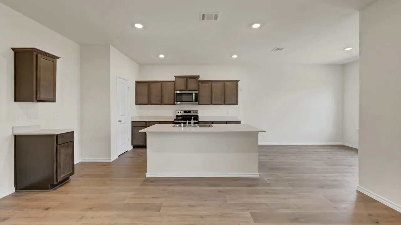 Open-concept kitchen with wood-finish flooring, dark wood cabinetry, and a central island with a sink