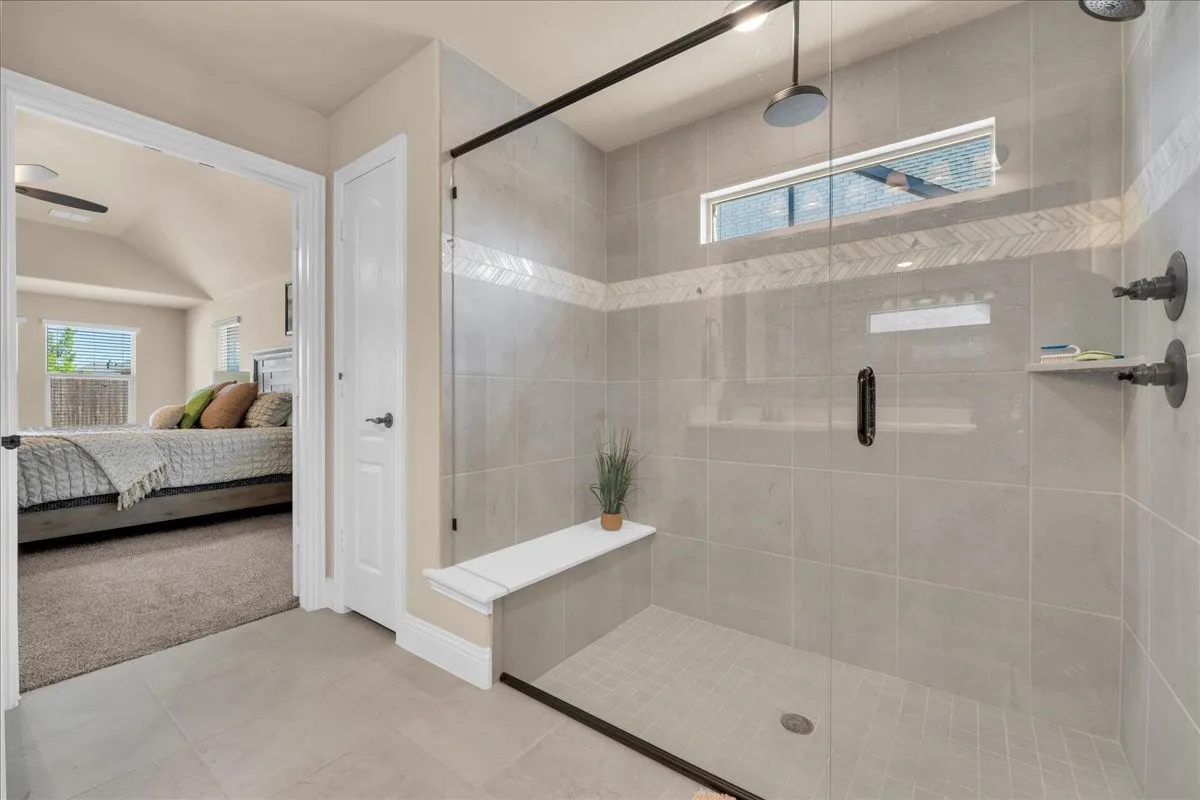 Spacious shower with glass enclosure, built-in bench, rainfall showerhead, and tile-finish walls