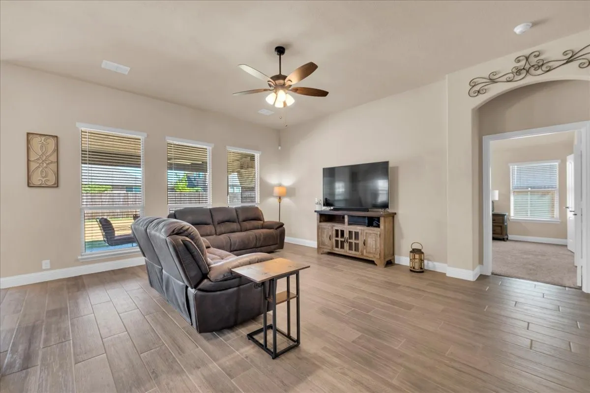 Wood-finish flooring, recessed lighting, ceiling fan, multiple windows with blinds, and an arched doorway