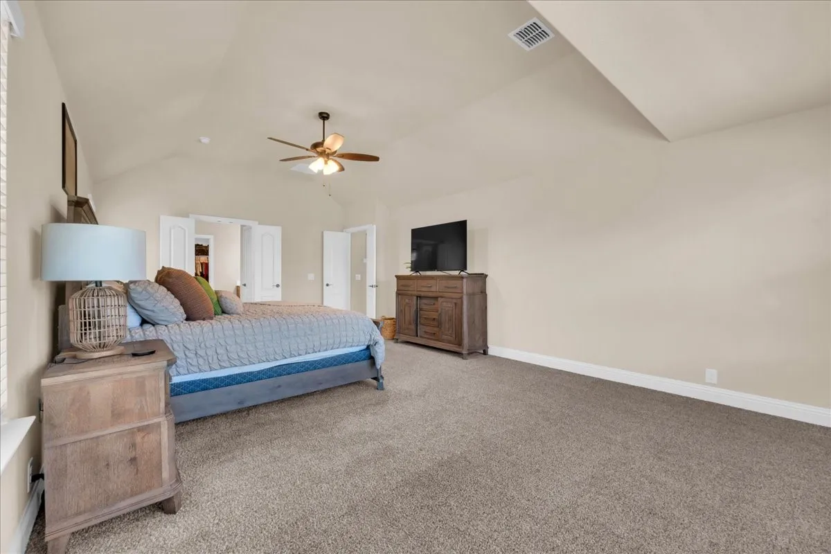 Vaulted ceilings, ceiling fan, plush carpeting, and light-toned walls
