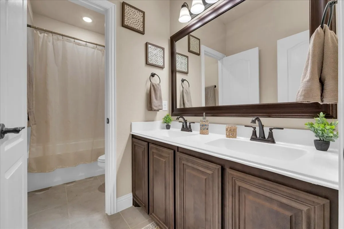 Double vanity with integrated sinks, dark wood-finish cabinetry, a large framed mirror, and matte black fixtures