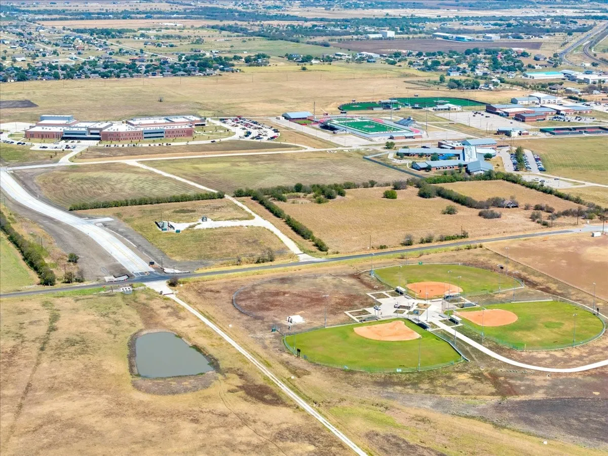 Expansive land parcel featuring open fields, a pond, and adjacent paved roads