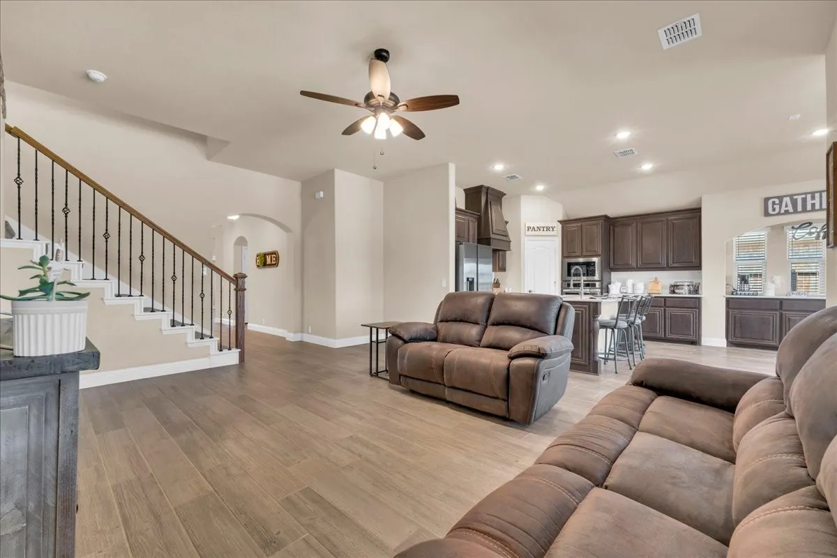 Wood-finish flooring, staircase with wrought iron balusters, recessed lighting, ceiling fan, and dark wood kitchen cabinetry