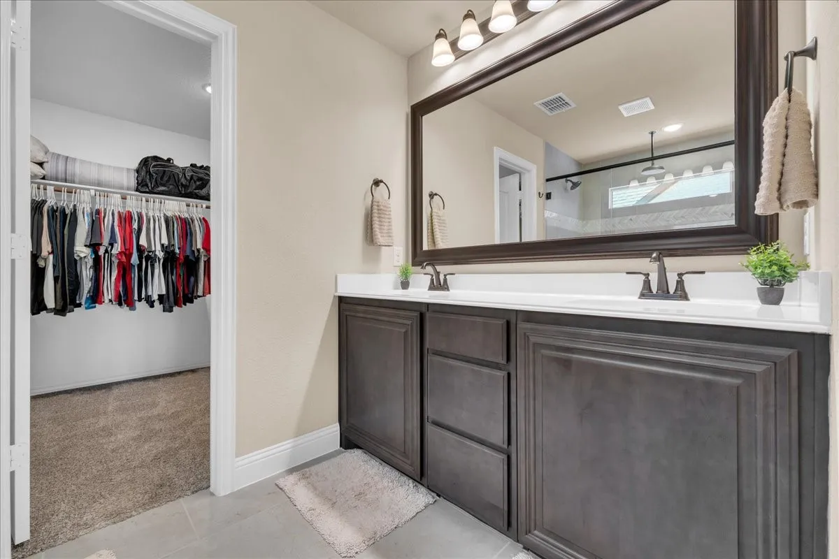 Dual vanity with dark wood cabinetry, white countertops, large framed mirror, and tile flooring