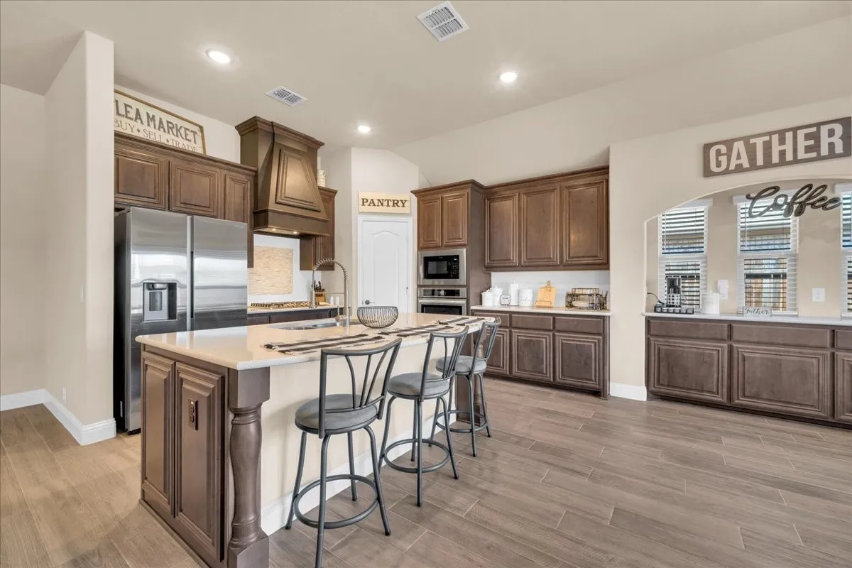 Spacious kitchen featuring an expansive center island, integrated stainless steel appliances, abundant cabinetry, and wood-finish flooring