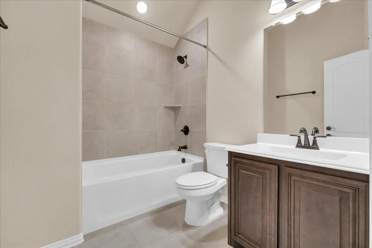 2nd floor Full Bathroom featuring a white bathtub with tile surround, dark bronze shower fixtures, a toilet, and a vanity with a white countertop and dark wood-finish cabinetry