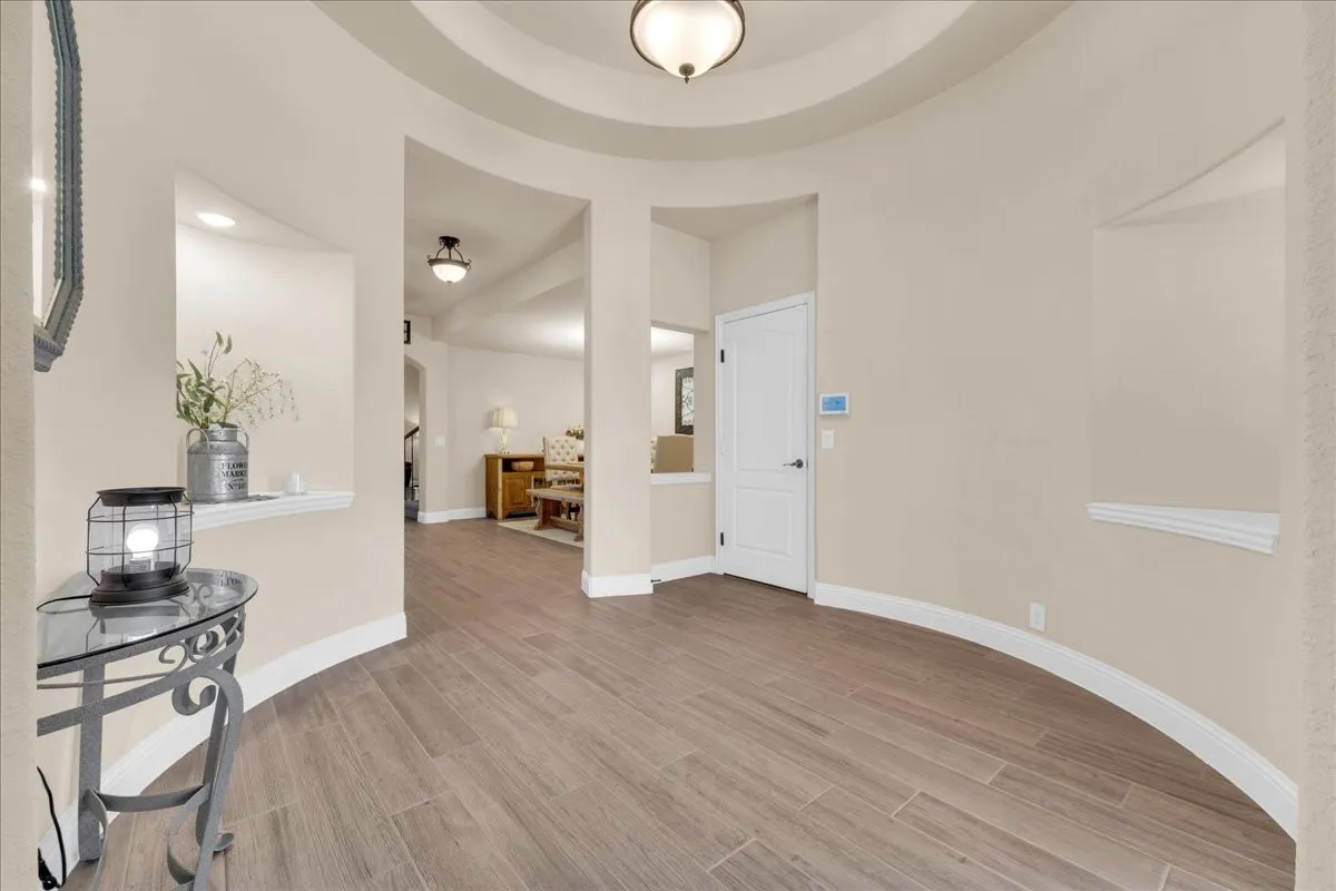 Curved entryway featuring wood-finish flooring, recessed wall niches, and a tray ceiling with a semi-flush mount light fixture