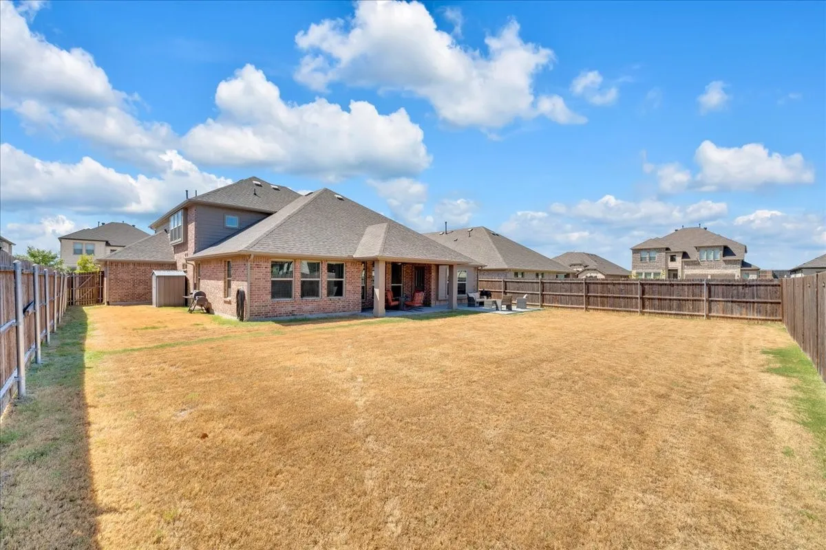 Expansive backyard with a full privacy fence, covered patio, multiple windows, and a brick exterior