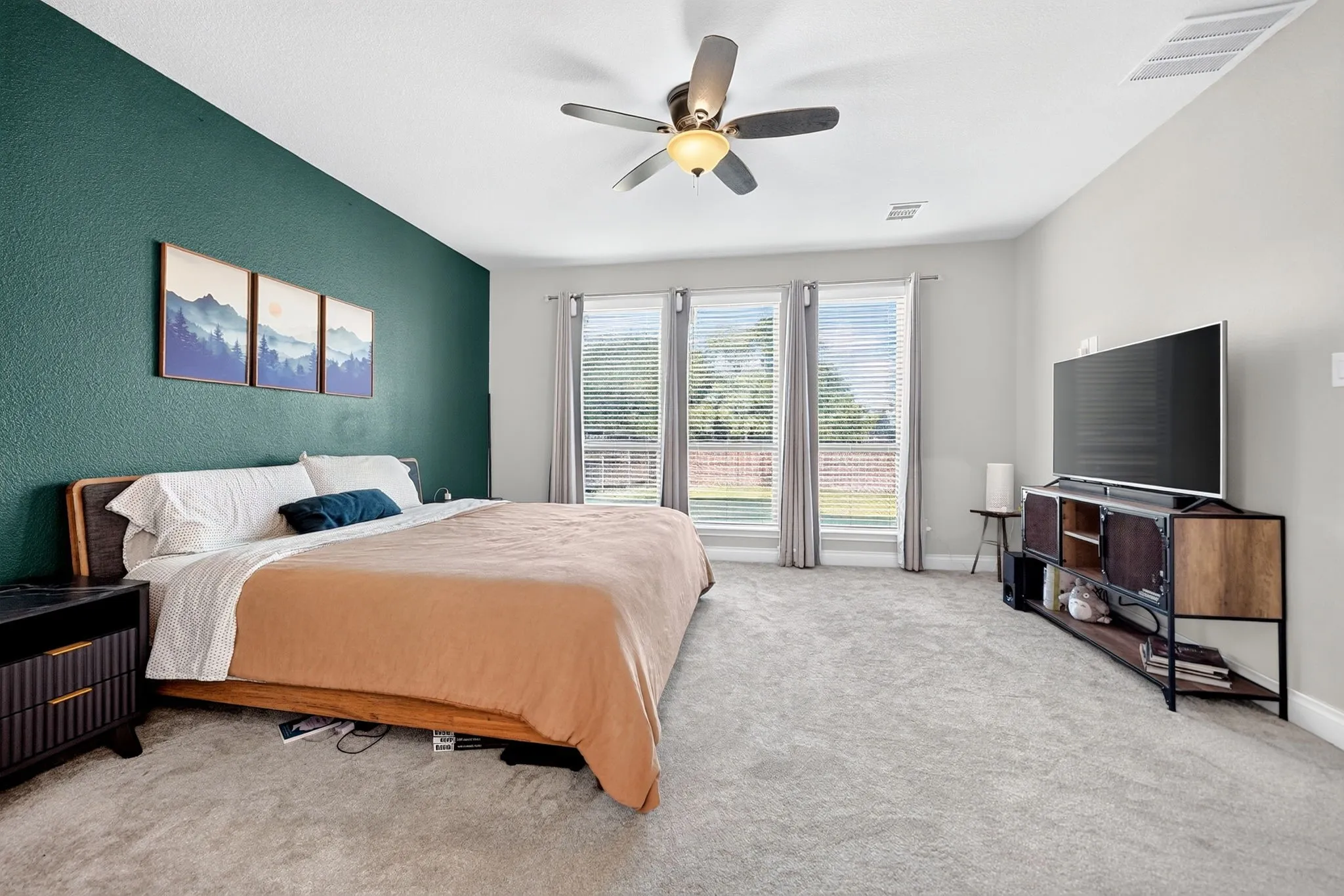 Textured accent wall, ceiling fan with integrated lighting, multiple windows with blinds, light-colored carpeting, and a built-in media console