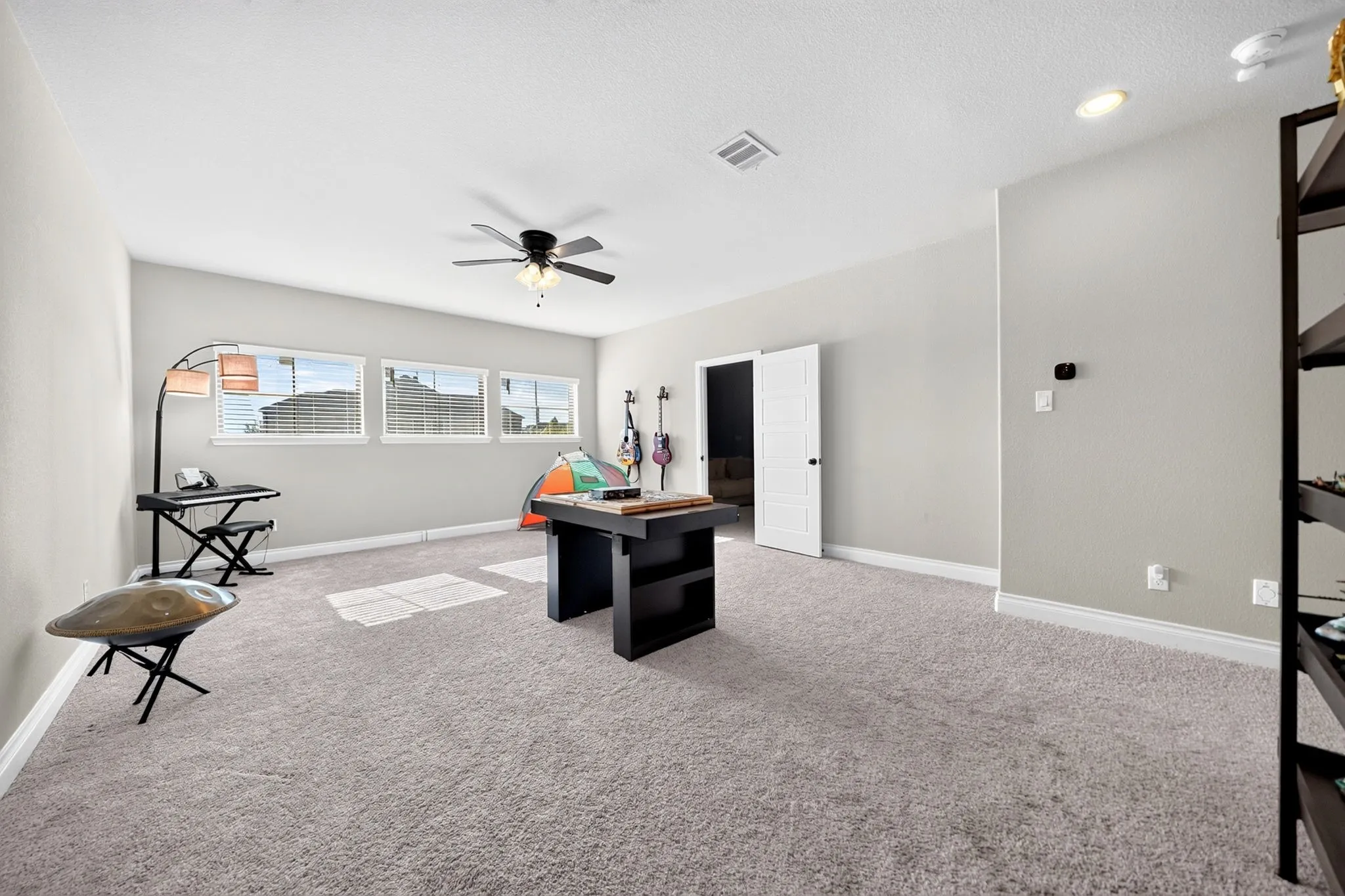Recessed lighting, ceiling fan, multiple windows, light gray carpeting, and a white paneled door