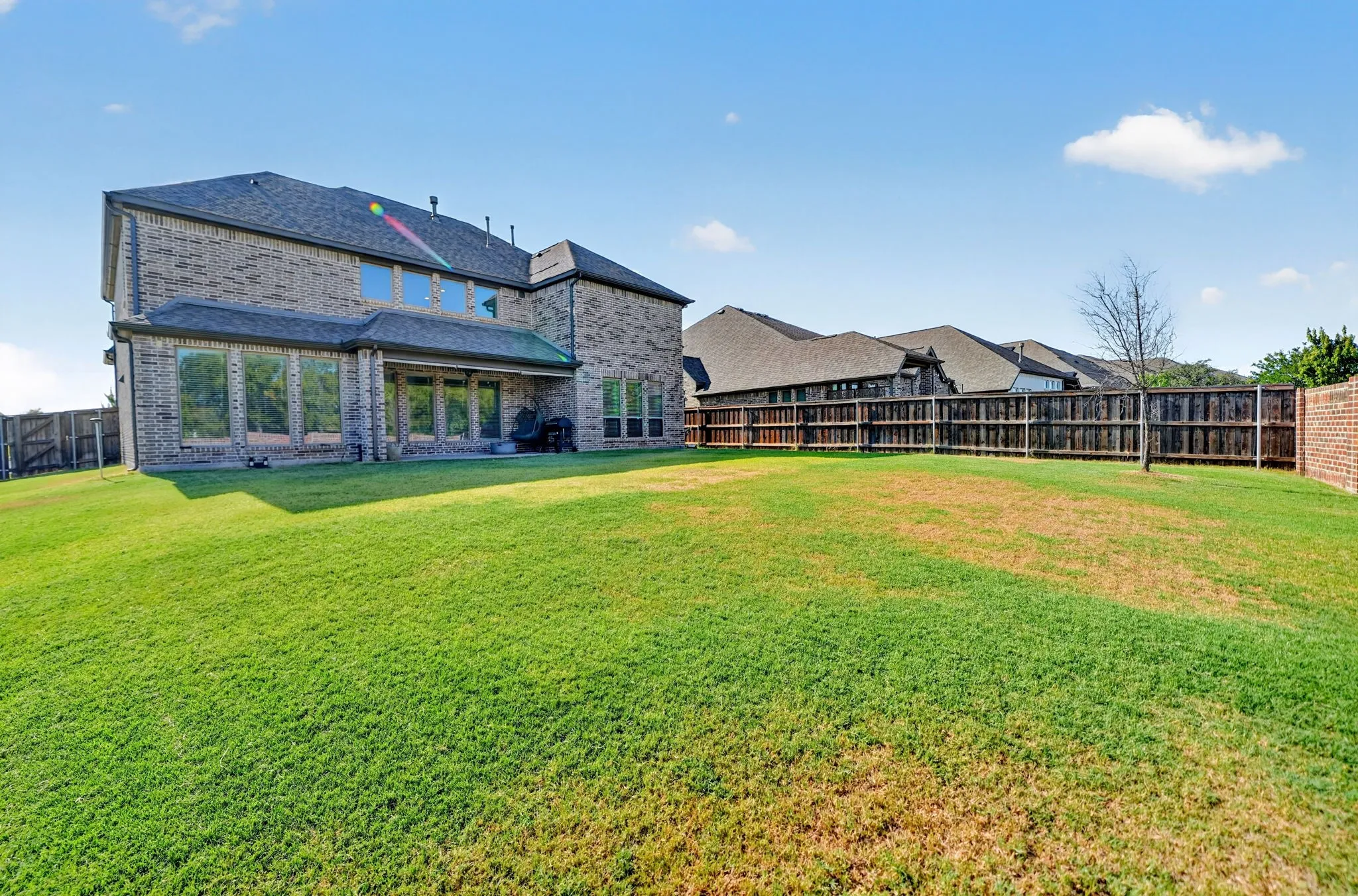 Spacious backyard featuring a brick and wood fence, large grassy area, and a home exterior with multiple windows