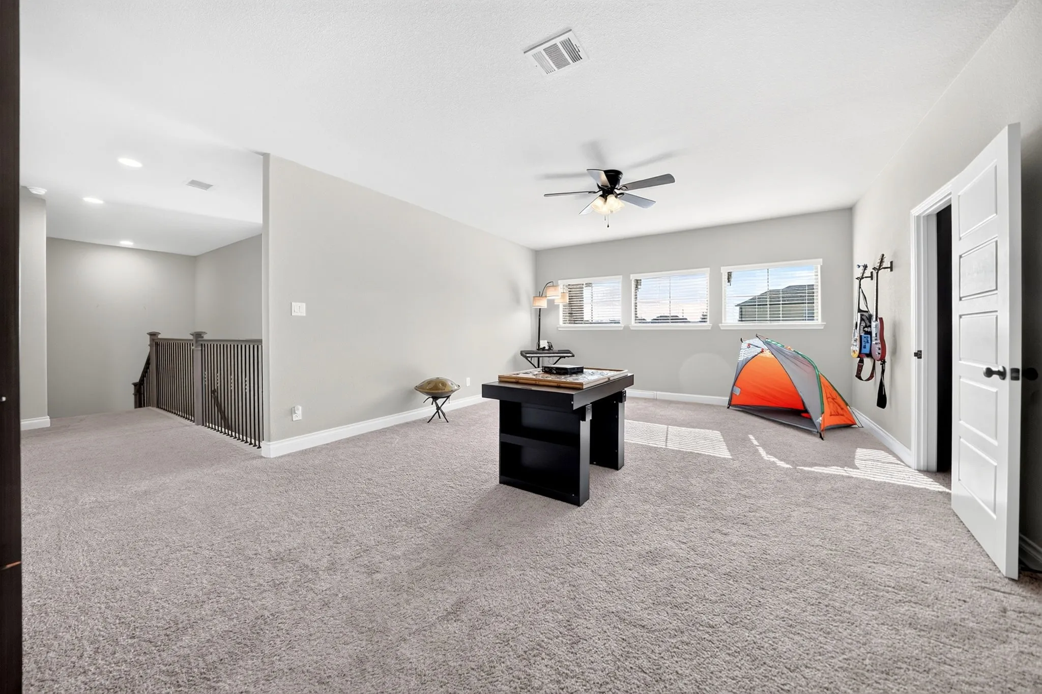 Spacious carpeted room featuring a ceiling fan, multiple windows, and a panel door